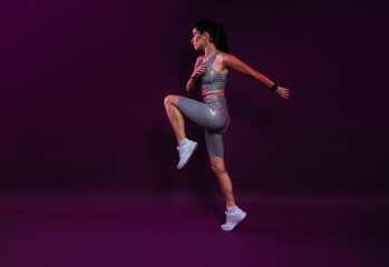 Full length of a young slim jogger practicing over a magenta backdrop. Female in silver fitness...