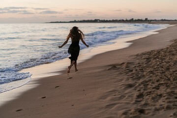 Young female in a dress running down a beach at sunset.