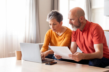 Portrait Of Serious Mature Spouses With Laptop Doing Paperwork Together