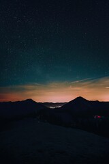 Vertical shot of a bright blue starry night sky over mountains