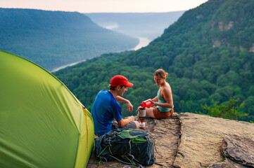 A young man and woman sit outside their tent at a clifftop campsite overlooking a river gorge in Tennessee