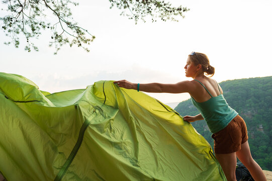 A young woman unfurls a tent rain fly atop a cliff overlooking a gorge in Tennessee