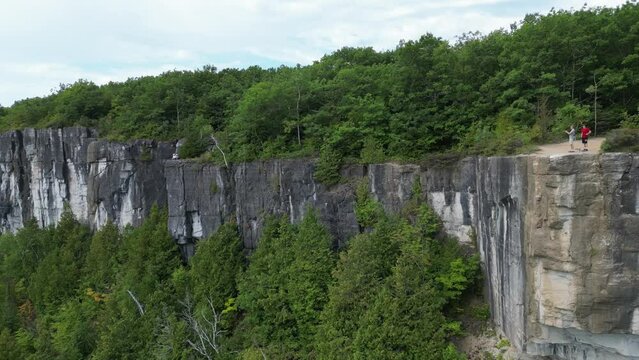 People taking pictures from the top of a cliff on Manitoulin Island. Huge cliffs and forest below from a birds eye view. Filmed with DJI drone