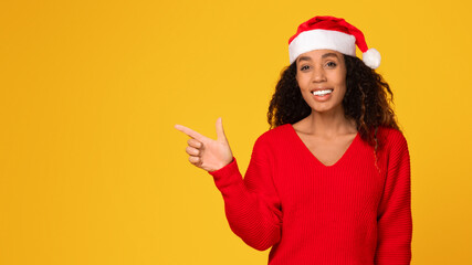 Smiling black woman in Santa hat points aside at copy space, panorama