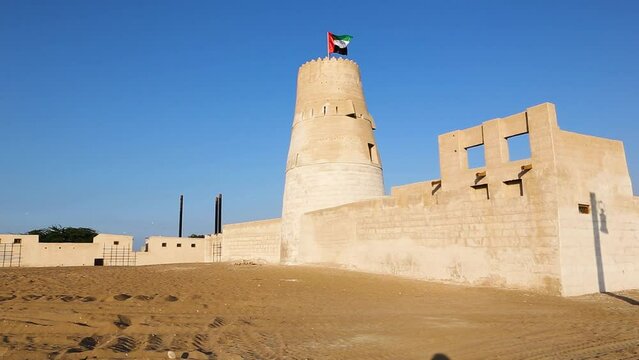 Stone arabic watchtower with waving United Arab Emirates National Flag in Al Jazirah Al Hamra haunted town in Ras Al Khaimah.
