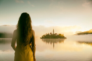 Woman in gray coat watching a sunrise among the fog on the shores of Lake Bled, Slovenia VII