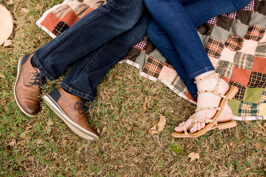 A romantic shot of a couple's feet - a man and a woman - lying on a quilted blanket in the fall season