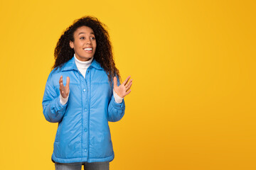 Black lady in jacket sees great offer, posing on yellow background