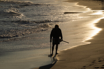 Silhouette of a man with metal detector on the sea at sunset