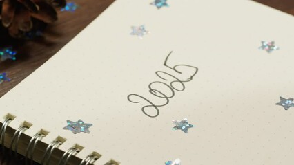 Hads writting some goals, purposes on list on wooden desk surrounded by Christmas decorations and gifts close-up. Vibes of winter holidays . 2024, 2025