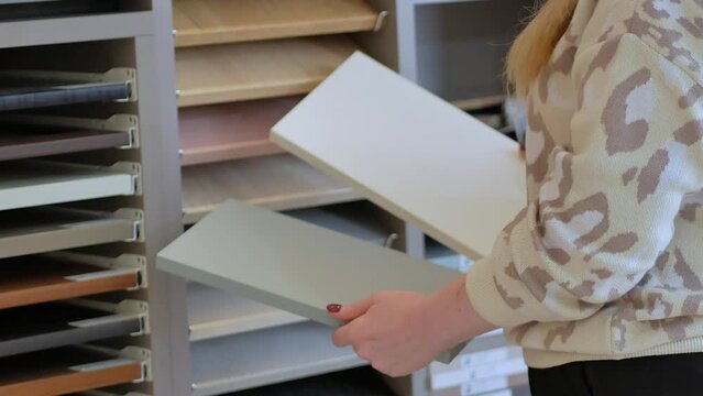 A female designer holds in her hands two samples of laminated chipboard decor in gray and white colors in a furniture store, applies two colors, compares.