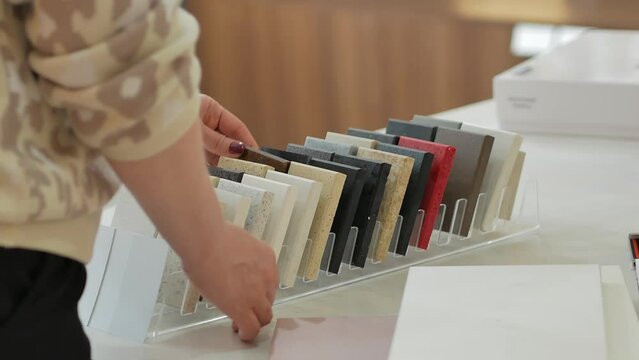 A woman with a beautiful manicure chooses a stone countertop for the kitchen in a furniture store, touches it with her hands and examines samples of materials