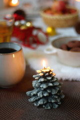 Cup of tea or coffee, glass of wine or juice, bowl of cookies, organic pomegranate, fluffy blanket, pine cones, various Christmas decorations and lit candles on the table. Christmas hygge concept.