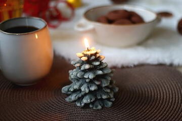 Cup of tea or coffee, glass of wine or juice, bowl of cookies, organic pomegranate, fluffy blanket, pine cones, various Christmas decorations and lit candles on the table. Christmas hygge concept.