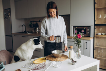 A cute big white and black dog helps her owner prepare a banana muffin with berries for breakfast....