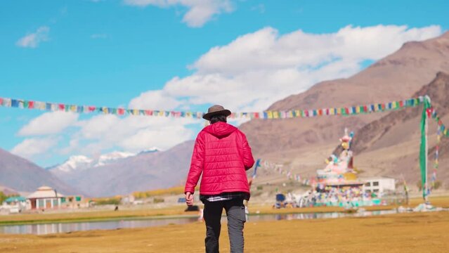 Rear View shot of an Indian tourist wearing hat walking in front of statue of Guru Padmasambhava besides the Sani lake in Sani village near Padum in Zanskar Valley, Ladakh, India. Tourist in Zanskar.