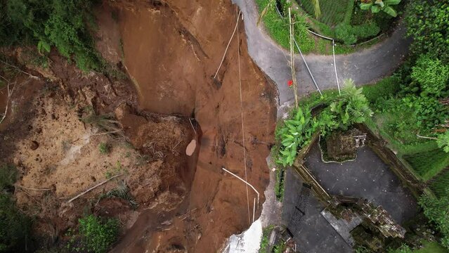 Recently there was dangerous landslide, road was destroyed and risk of house collapse still exist. Aerial shot of local cataclysm at central Bali, camera look down and spin, flying up over event area