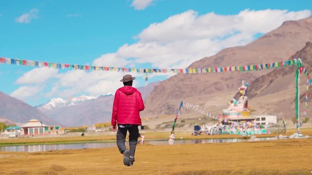 Rear View shot of an Indian tourist wearing hat walking in front of statue of Guru Padmasambhava besides the Sani lake in Sani village near Padum in Zanskar Valley, Ladakh, India. Tourist in Zanskar.