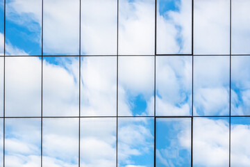 Abstract or graphic photo of the sky with clouds seeming to continue into a building with reflective squares of glass - obrazy, fototapety, plakaty