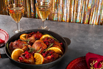 Christmas baked chicken with cranberries and oranges in a frying pan and two glasses of champagne on a festive table