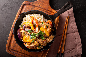 Asian pork with vegetables and glass noodles in a pan on the black background