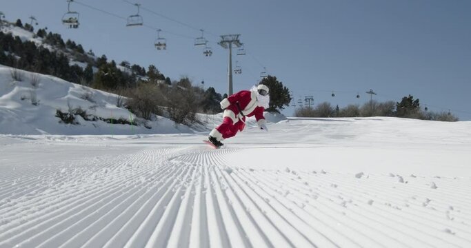 A man dressed in a Santa suit snowboarding down a ski slope. Snowboarder doing hand drag on fresh snow surface. Festive spirit of Christmas or New Year holidays