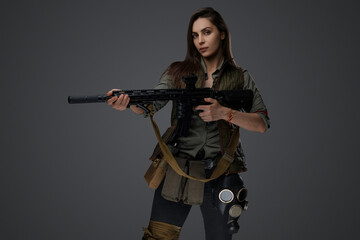 Middle Eastern-looking woman dressed in survivalist clothing posing with a rifle against a gray background, portraying strength and resilience