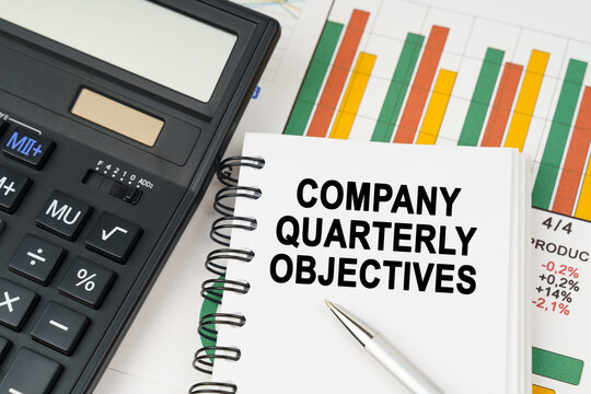 On business charts there is a calculator, a pen and a notepad with the inscription - COMPANY QUARTERLY OBJECTIVES