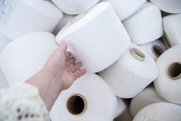 the hand touches large bobbins of linen threads for white fabrics .Flax processing plant, fabric...