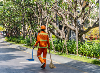 janitor in orange uniform walks with broom and dustpan in hands