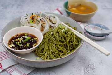 Vegan green tea noodles and dipping sauce, daikon salad. White bowl, chopsticks, miso soup