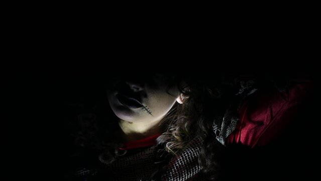 Brunette girl in Halloween style. A woman on a black background, a flickering light on her face, a scary scene. Terrible darkness. Depression, suffering, crime. Black Carnival, in the basement.