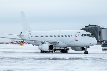 Obraz premium White passenger jet plane at the boarding bridge at winter airport apron