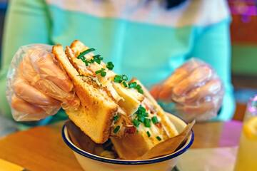 Hands girl special gloves holding square sandwich chicken, cheese and green onions