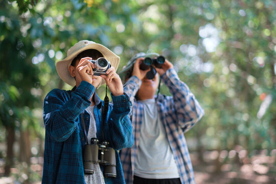 Two young boys in the forest hiking and camping. learning about wildlife, using a camera, taking pictures and binoculars to search for animals with friends. Happy smiling excited summer vacation.