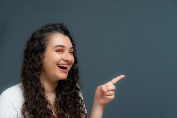 Smiling female in the studio showing free empty space with her finger in a confident manner