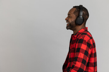 Profile of happy black bearded man in headphones wearing red checkered shirt listening to music
