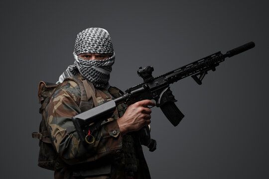 Militant from the Middle East, dressed in a white keffiyeh and camouflaged field attire, wielding an automatic rifle, set against a neutral gray backdrop - Powered by Adobe