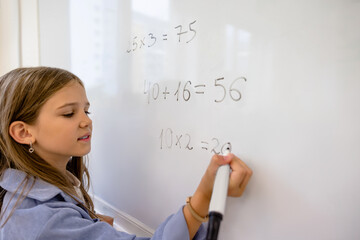Cute fair-haired schoolgirl writing on the board and looking concentrated