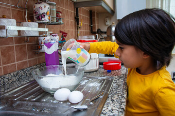 Little girl adds milk to flour in a bowl