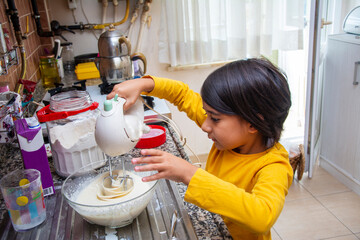 Little girl mixes the cake ingredients with a mixer after they are prepared.