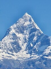 Fototapeta na wymiar Incredible aerial shot of a majestic snow-covered mountain peak against a bright blue sky