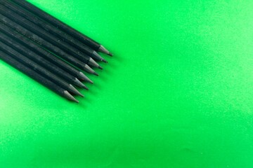 Assortment of black pencils laid out on a green background