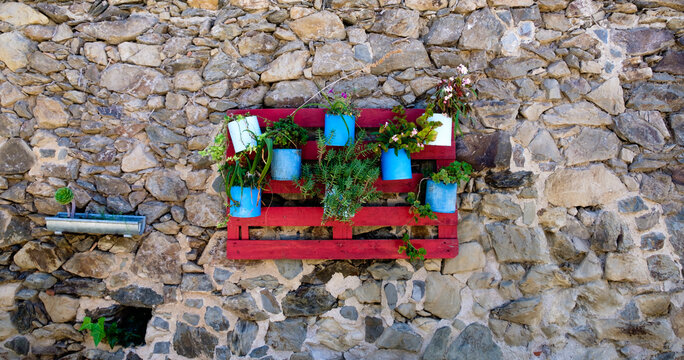 macetas azules con flores verdes colgada sobre armazon de madera roja en pared de piedra