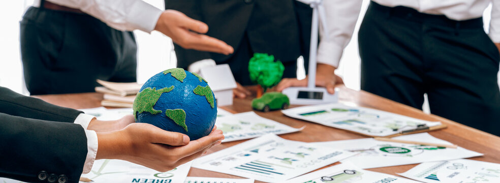 Businessman hand holding paper Earth with business people on meeting in office, planning and implementing eco-friendly ideal for corporate policy to reduce CO2 emission and save earth. Trailblazing