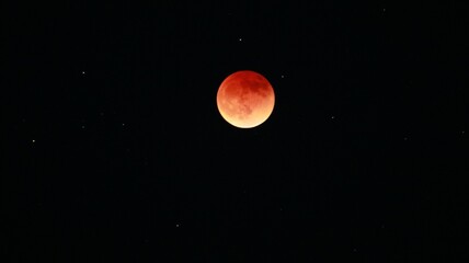 Blood-red eclipse of the moon in the night sky with shining stars