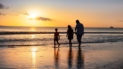 Fototapeta na wymiar Uma família em contraluz, passeando na praia com um lindo pôr-do-sol. Conceito de férias.