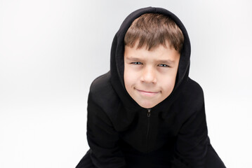 A young cheerful boy in a sports suit with a hood on a light background is smiling, resting after...