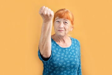 An older woman is smiling and waving her fist at someone, as if threatening someone, but she has...