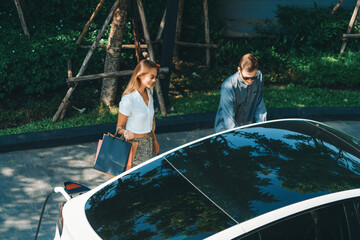 Young couple travel with EV electric car charging in green sustainable city outdoor garden in...